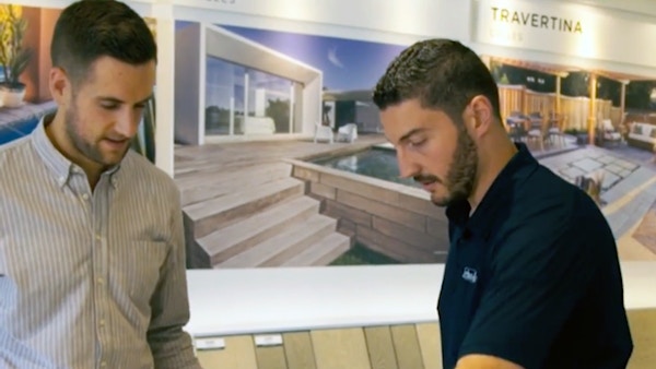 Two men are standing in a room with photos on the wall behind them.