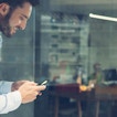 A man on his phone stands behind a glass window. There is an office in the background.