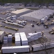 There is a wide shot of a warehouse with trucks and pallets outside.