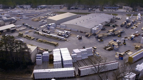 There is a wide shot of a warehouse with trucks and pallets outside.