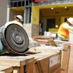 There is a closeup on a piece of construction equipment. In the background, construction workers work on a project.