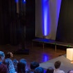 Two people are on a stage with people in the audience watching.