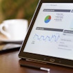 A tablet sits on a desk displaying graphs and charts.
