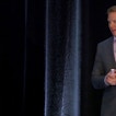 A man presents in front of black curtains.