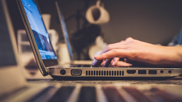 An unseen person types on a laptop.