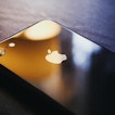 An apple phone sits facedown on a black surface with the apple logo facing upward.