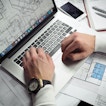 A pair of hands works at a computer with house layout plans displayed on the screen.