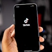 There is a phone with the Tiktok app being held by a hand.