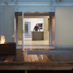 There is an open door leading into a house with a person standing behind a counter. Next to the door is a fire.