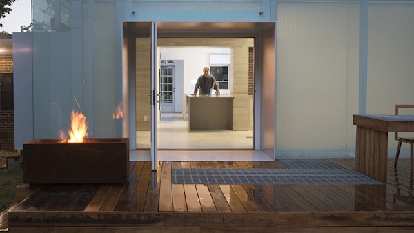 There is an open door leading into a house with a person standing behind a counter. Next to the door is a fire.