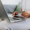 A person is sitting down, shopping online from a laptop. They have a credit card and are entering information on the computer.