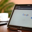 A tablet, a phone and a white tea cup are sitting on a table.The tablet has Google pulled up.