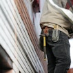 A person wearing black pants, a tan shirt and a tool belt is on a job site.