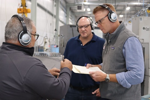 Three people are in a warehouse, and they are looking at a piece of paper together.