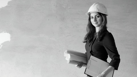 An industry professional wearing a hard hat and holding a clipboard and rolled-up pieces of paper.