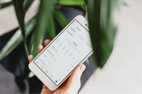 A person is holding their smartphone, reading data and insights from their Instagram account.