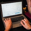 There is a man with his face obscured from behind typing on a laptop.