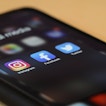 A phone sits against a pale background. The app icons for Instagram, Facebook, and Twitter are displayed.