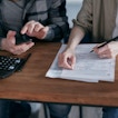 Two people are sitting at a table with a calculator and paper.